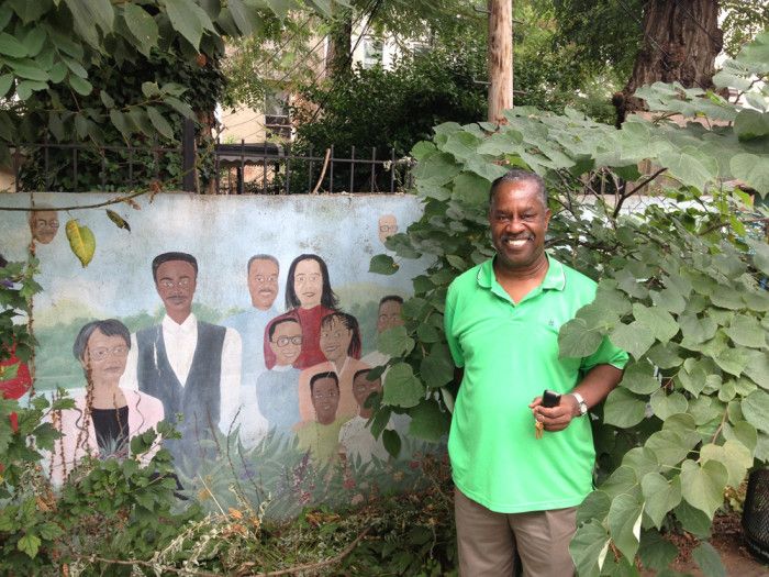 Demetrice Mills stands in front of a mural depicting Demetrice (in light blue) and other contributors to the Classon/Ful-Gate Community Association Garden.