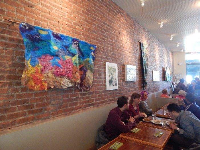 Neighbors eat brunch under the exhibit's artwork, including Madeline Sorel's Nuno felt piece, far left.