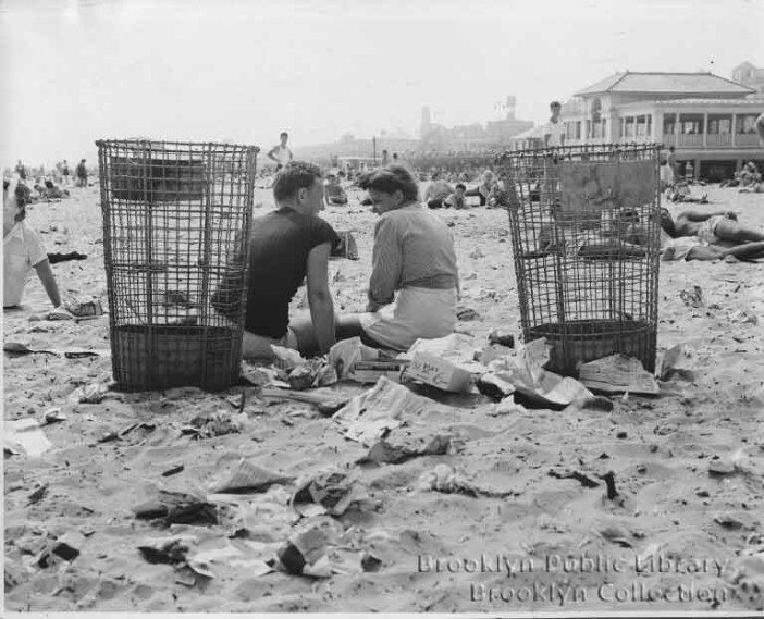 a couple sits on the sand amidst trash in coney island in 1946