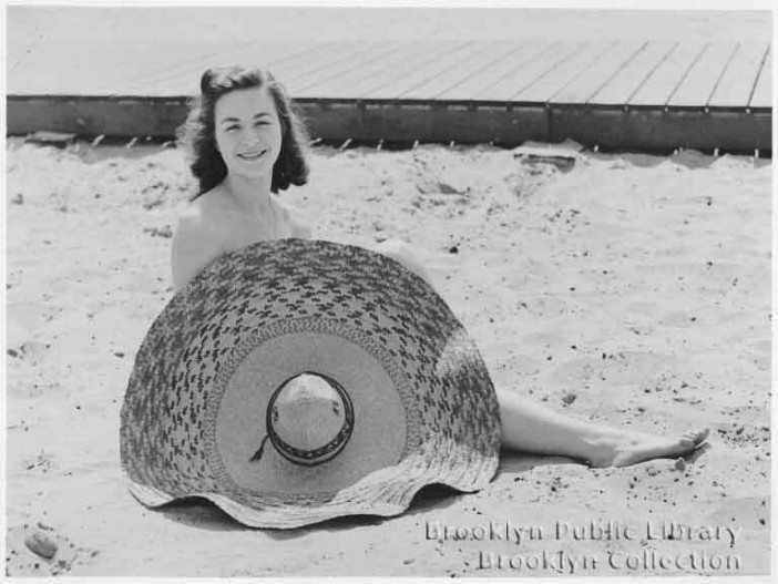 a woman sits obscured by a sombrero on the coney island beach