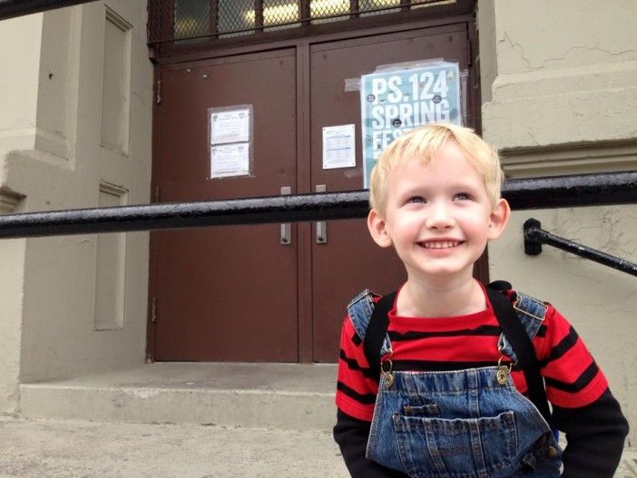 a child smiles as he is about to enter a school building