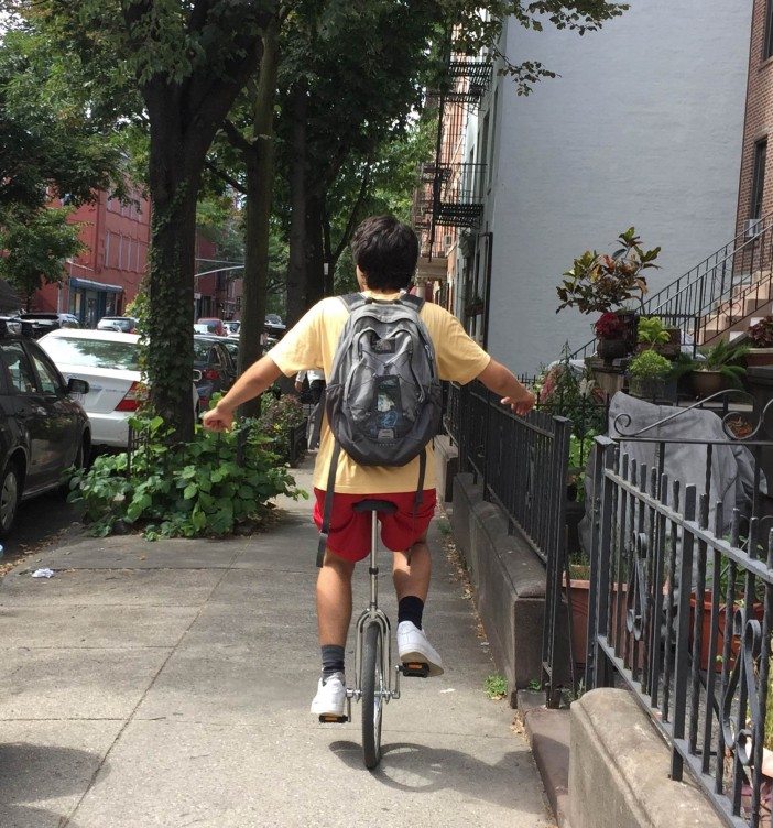 a boy rides a unicycle down the sidewalk